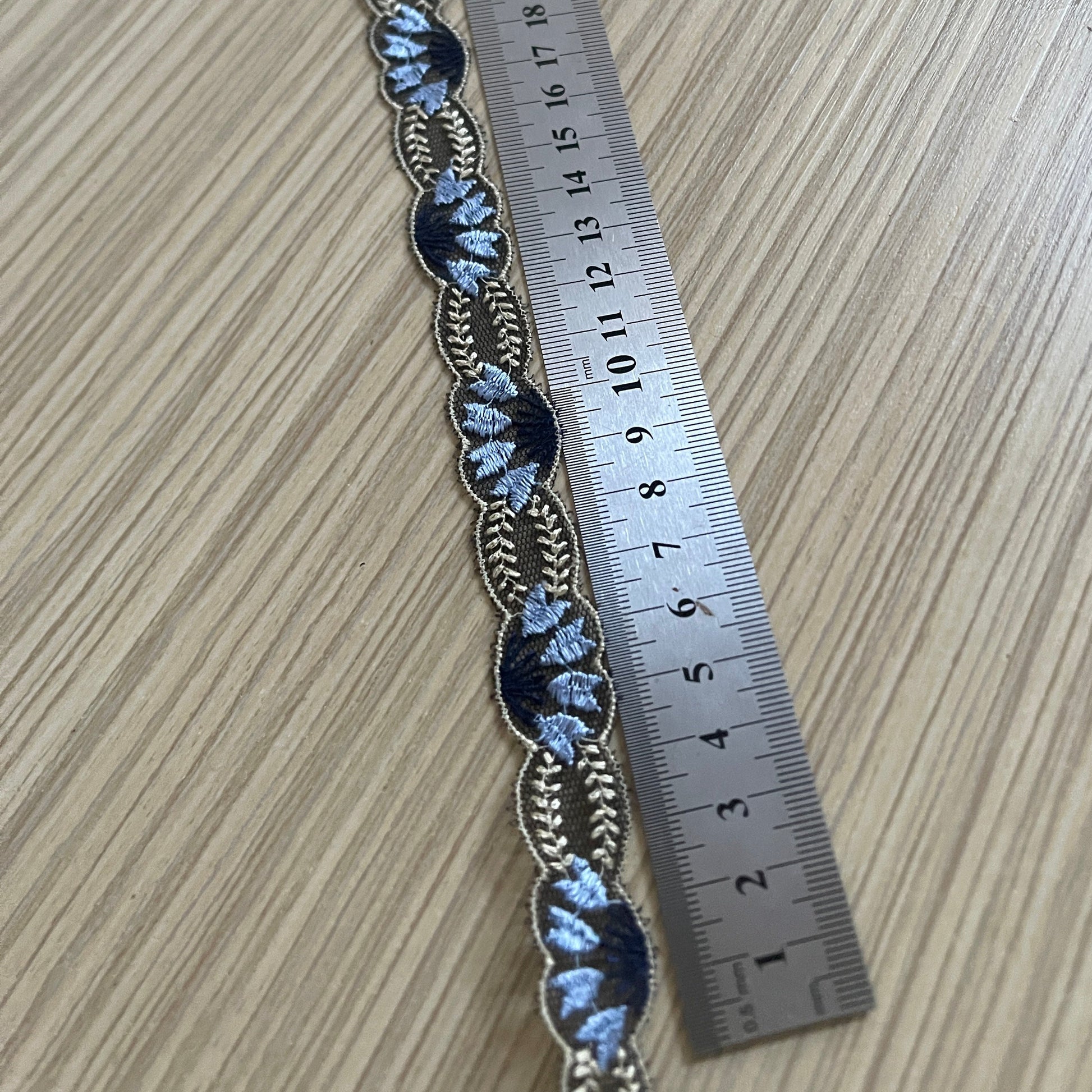 Image d’un ruban de dentelle brodée de 2 cm, bleu foncé avec accents beiges, disponible chez Šarlotes audumi